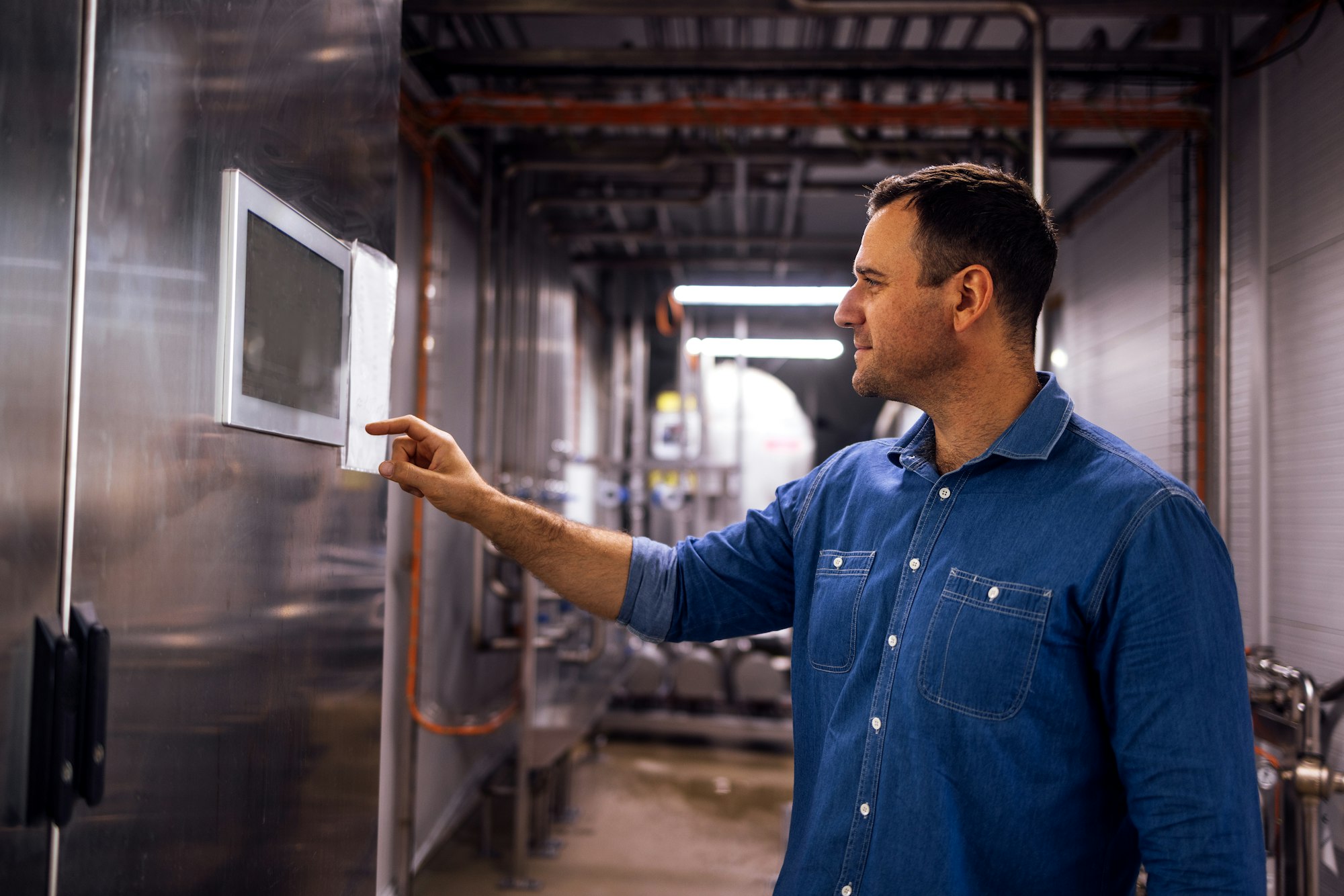 Young man sets necessary parameters on display on equipment in cheese factory