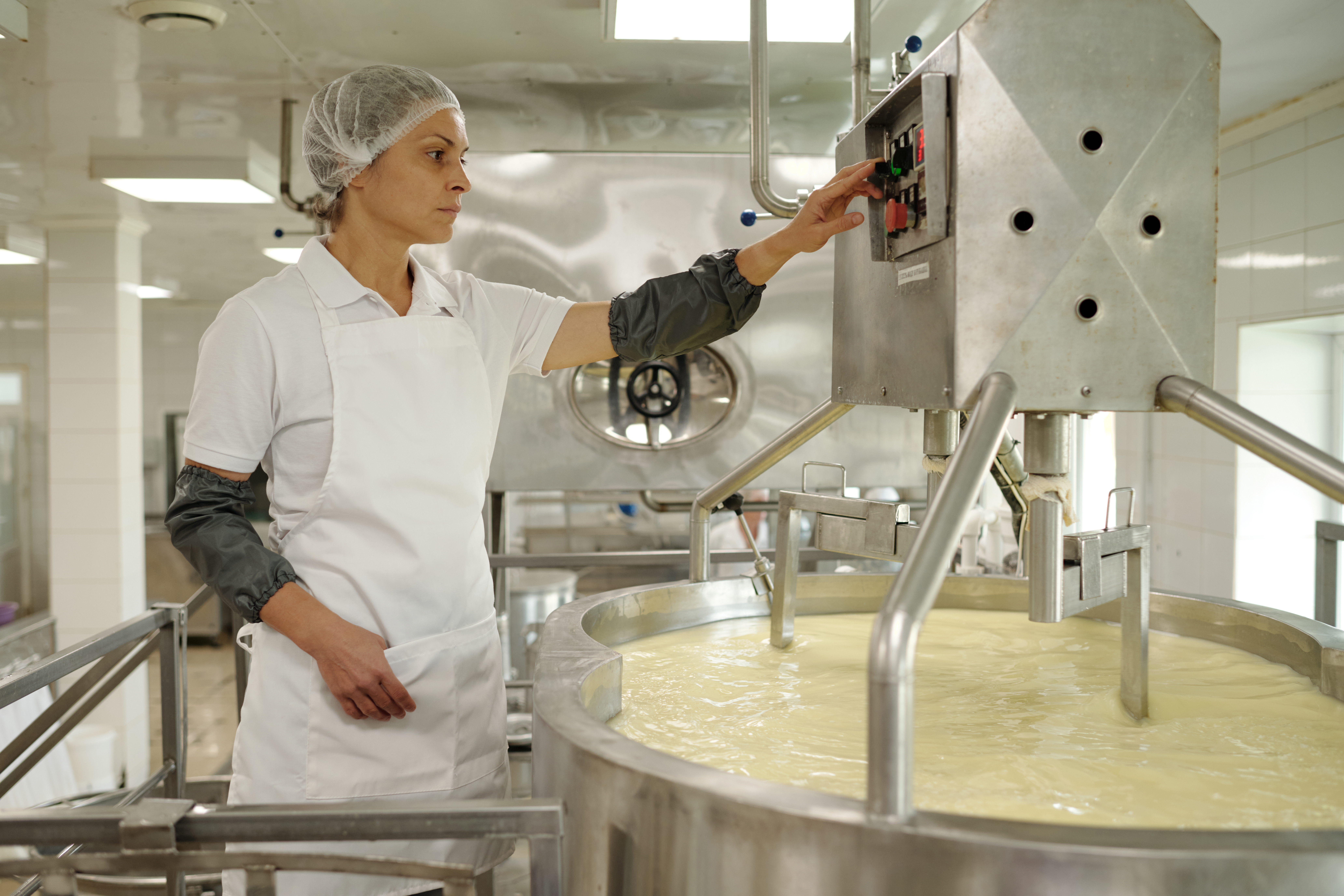 Dairy membranes, dairy processing, Woman in white uniform monitoring large industrial cheese production machine in production facility. Dedicated worker ensuring quality control in cheese-making process